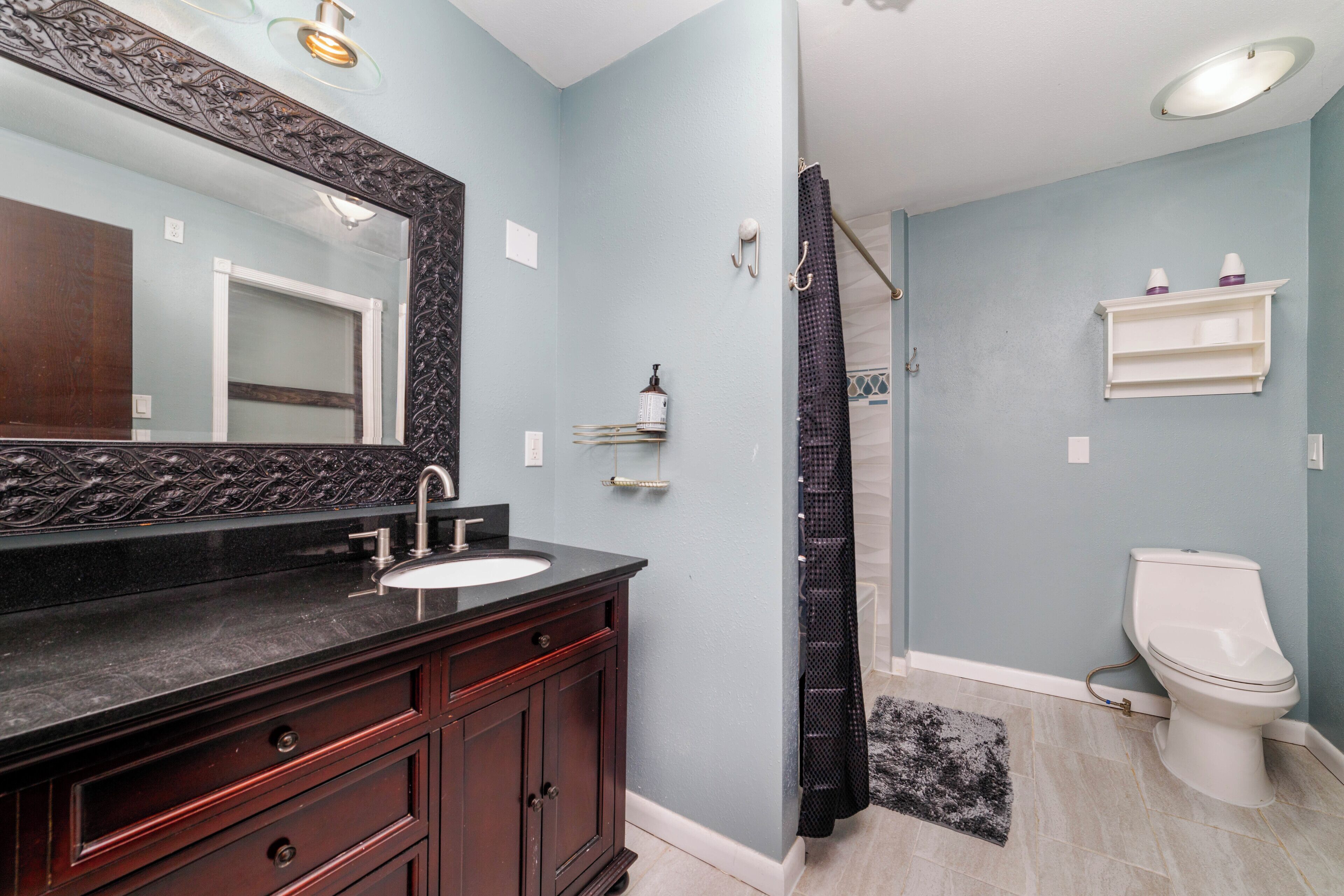 A bathroom with a dark wooden vanity, a white toilet, and a shower curtain.