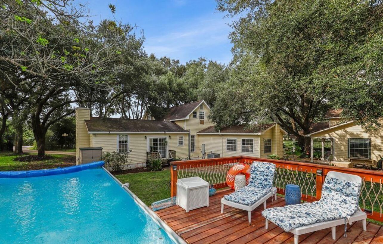 A backyard with a swimming pool, wooden deck, and lounge chairs.
