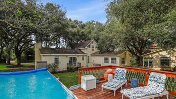 A backyard with a swimming pool, wooden deck, and lounge chairs.