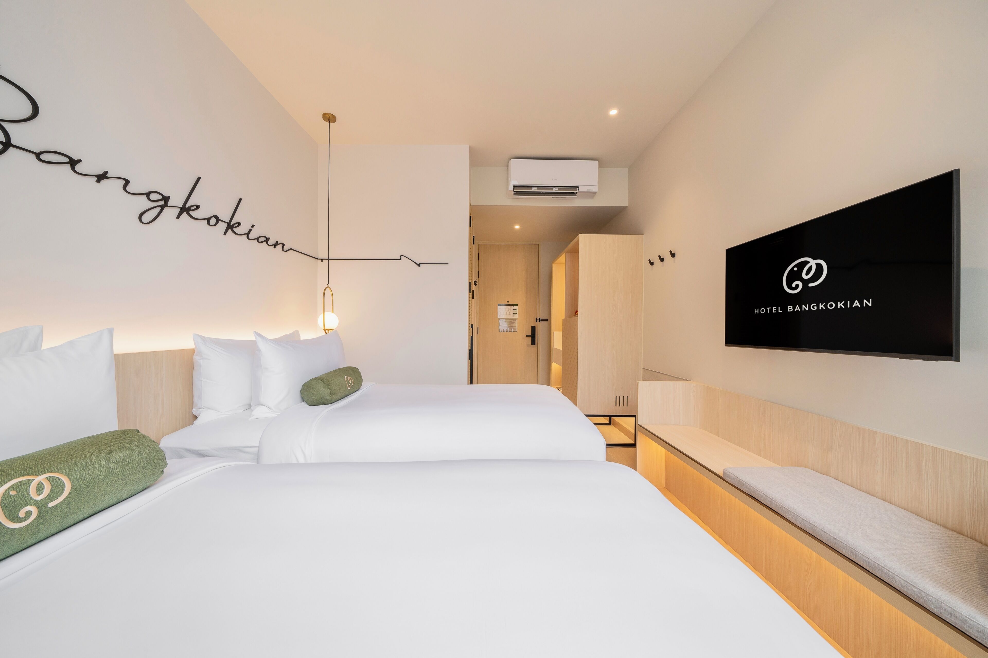 A hotel room with a bed, a TV, a wall-mounted air conditioner, and a hallway leading to a bathroom.