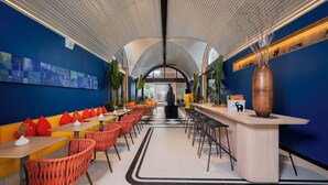 Un restaurante moderno con una barra larga, sillas rojas y una pared azul decorada con obras de arte.