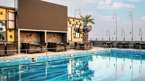 Zona de piscina con sillones y mesas, una piscina cristalina y vistas del horizonte de la ciudad.
