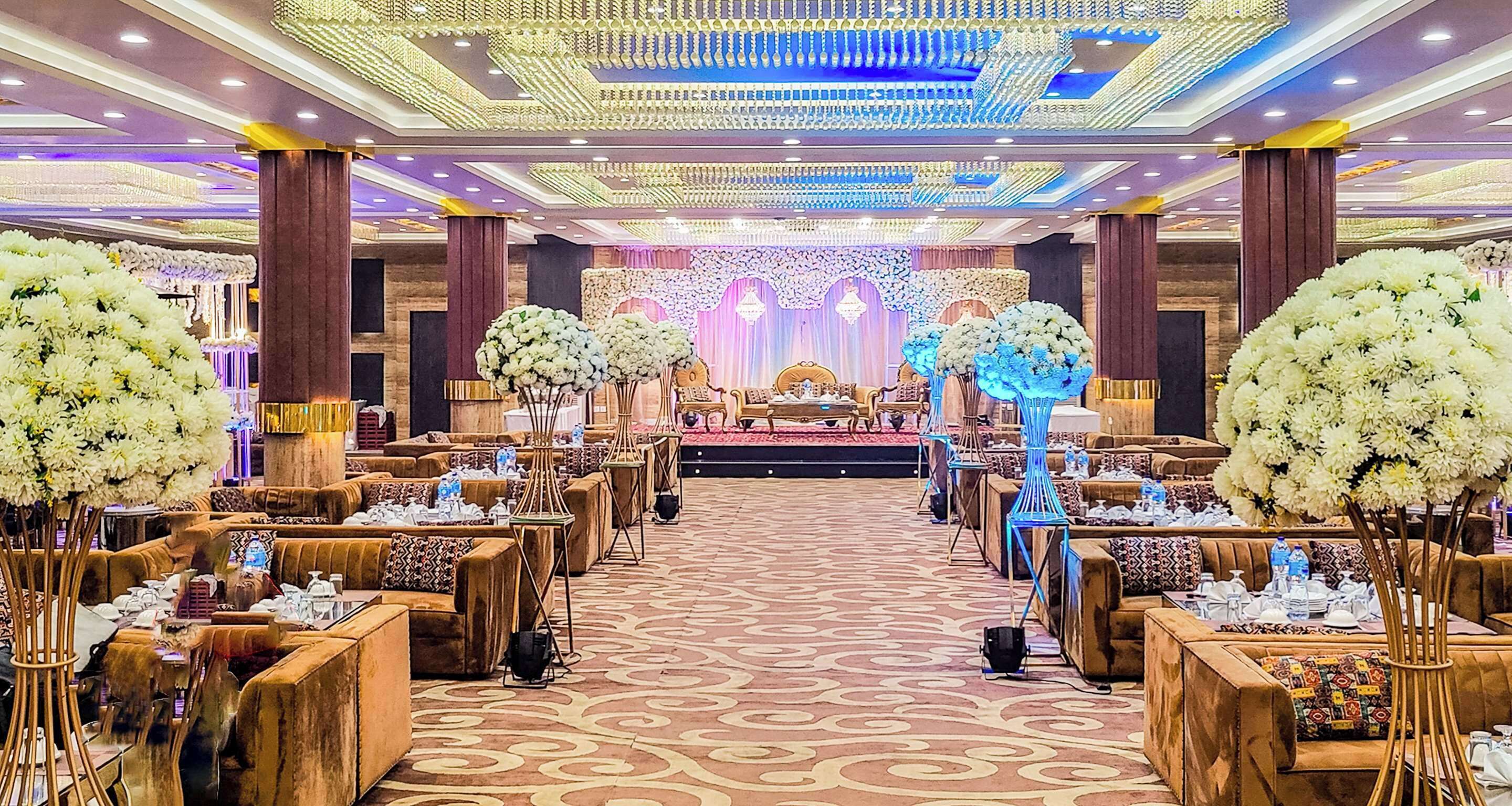 A banquet hall with rows of seating, a stage with floral decorations, and a patterned carpet.