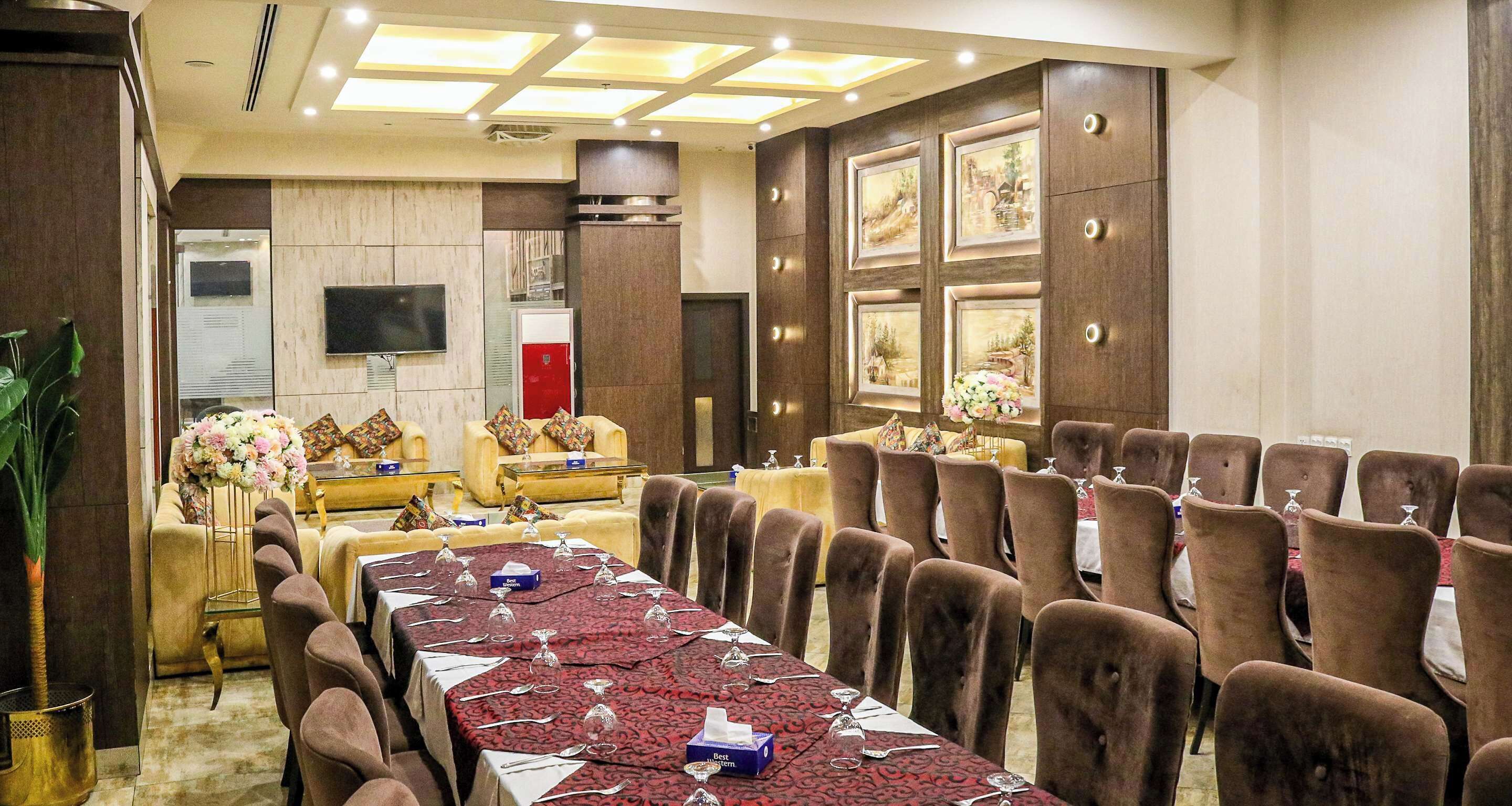 A conference room with a long table, brown chairs, a sofa, and a TV screen.