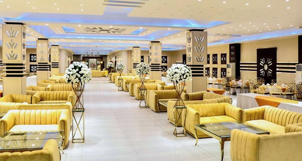 Un amplio vestíbulo de hotel con filas de sofás y sillones amarillos, pilares decorativos y un arreglo floral central.