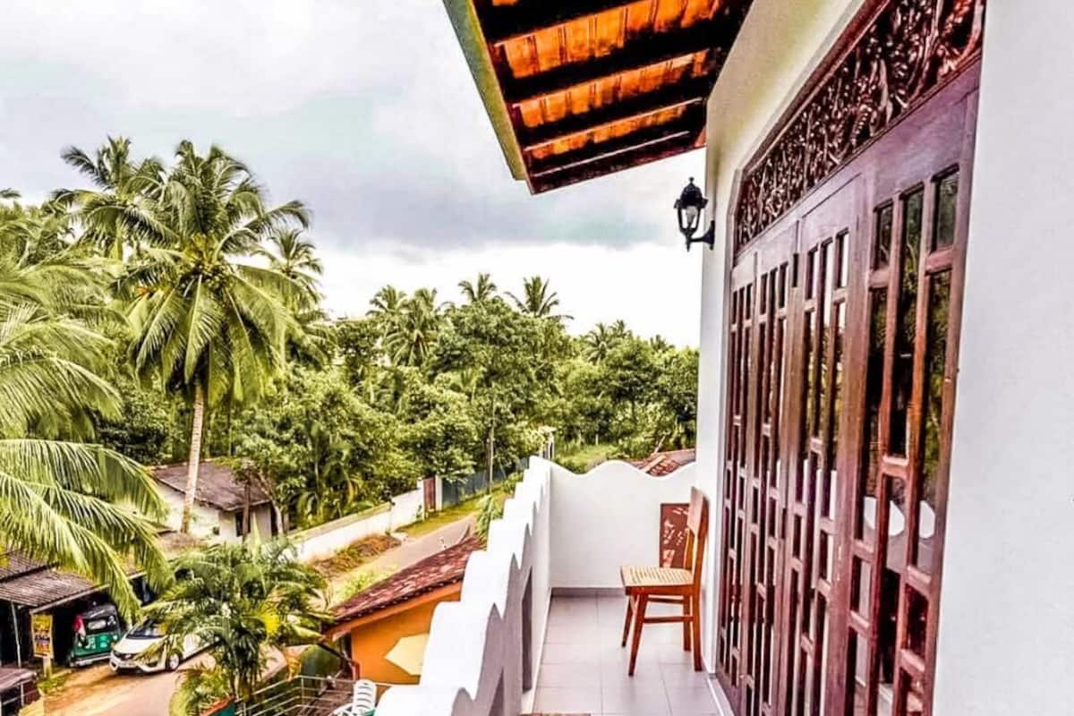 A balcony with a pool, wooden furniture, and a view of palm trees and a road.