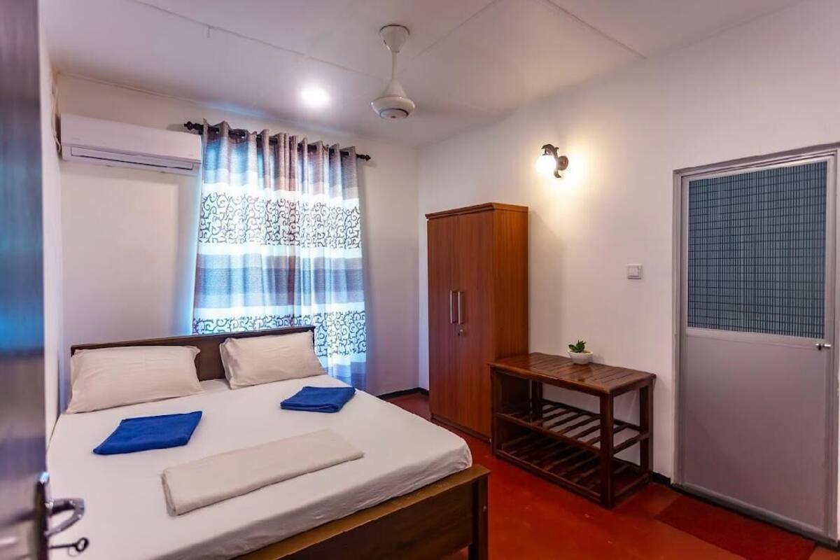 A hotel room with a bed, a wardrobe, a small table with a plant, and a window with curtains.