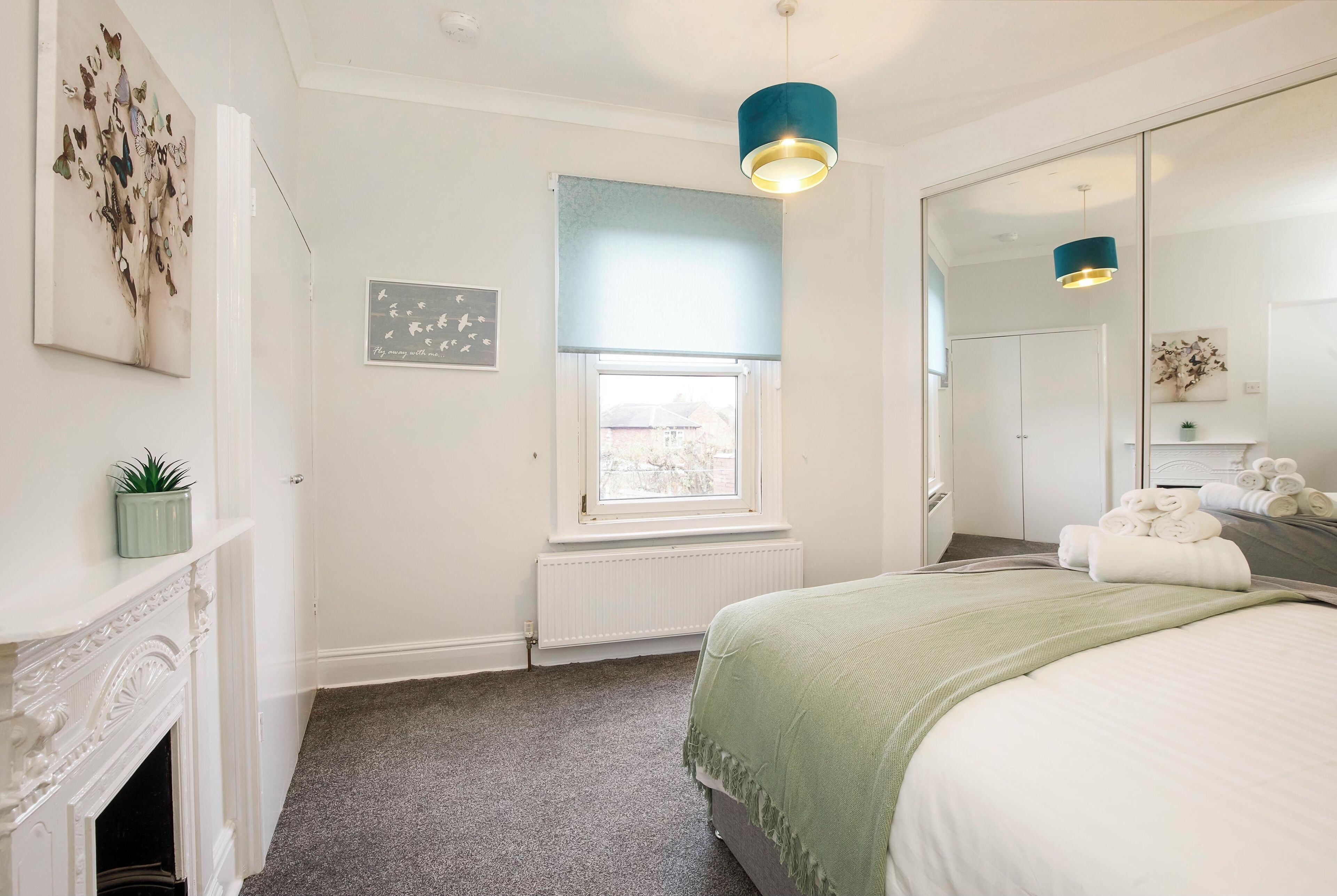 Een slaapkamer met een bed, een raam met zonwering, een open haard en een spiegel.