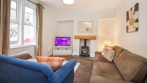 Una sala de estar con sofá, televisión, chimenea y ventana con cortinas.