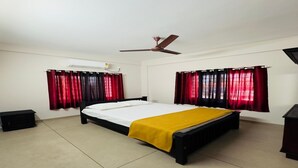Quarto com cama, ventoinha no teto e duas janelas com cortinas vermelhas.