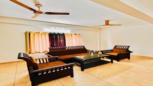 Uma sala de estar com sofá, duas poltronas, uma mesa de centro e duas ventoinhas de teto.