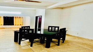 Uma sala de jantar com mesa de vidro e cadeiras pretas, um ventilador de teto e vista para um espaço com cortinas.