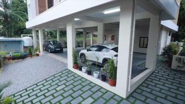 Área de estacionamento coberta com dois carros, plantas em vasos e calçada pavimentada.