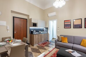 A modern living room with a grey sofa and a dining area with a table set for four. - Lovely Flat In Genova Historic Center Apartments (Genoa)