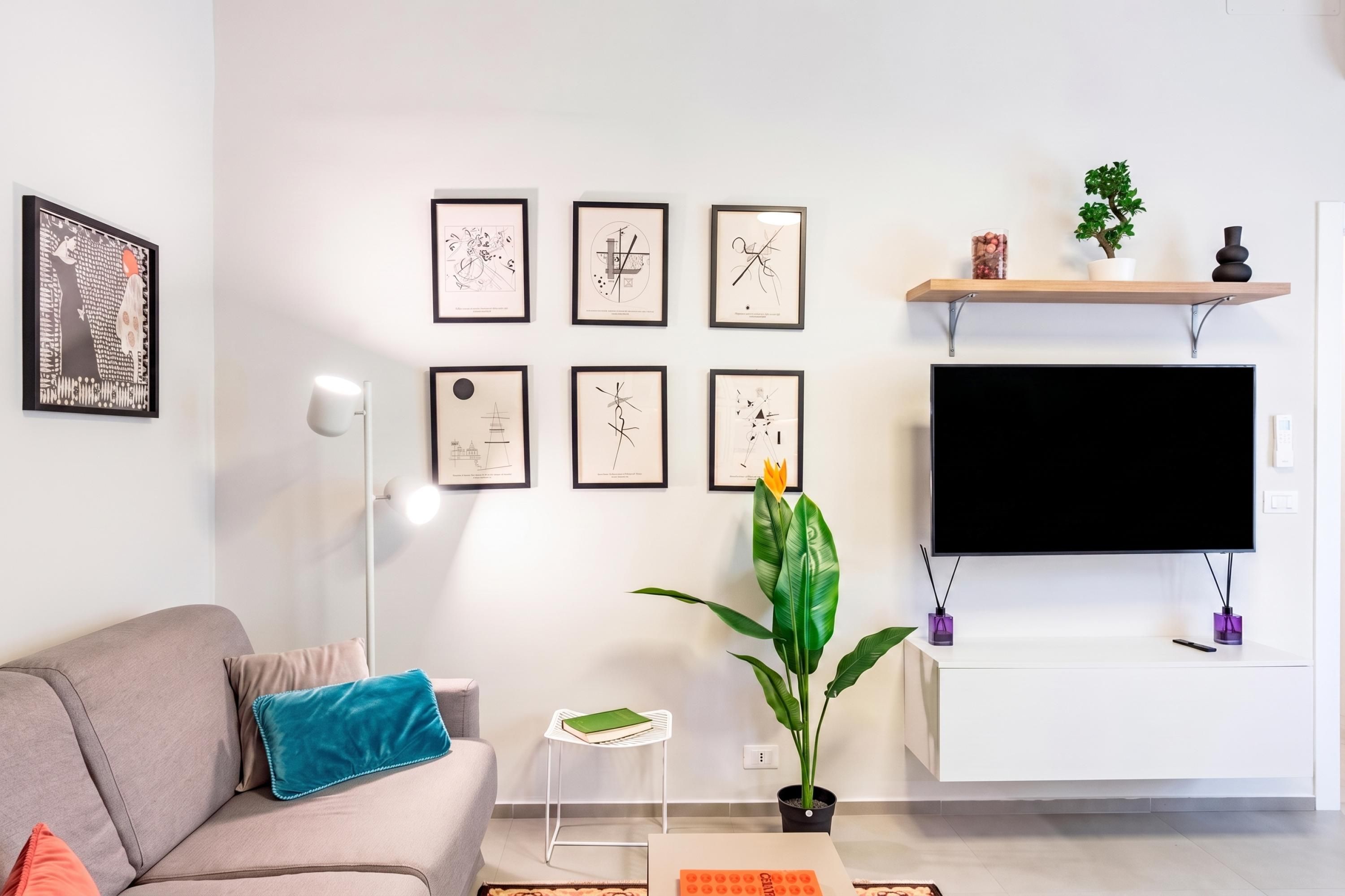 A modern living room with a sofa, a coffee table, a floor lamp, a TV mounted on the wall, and framed artwork.