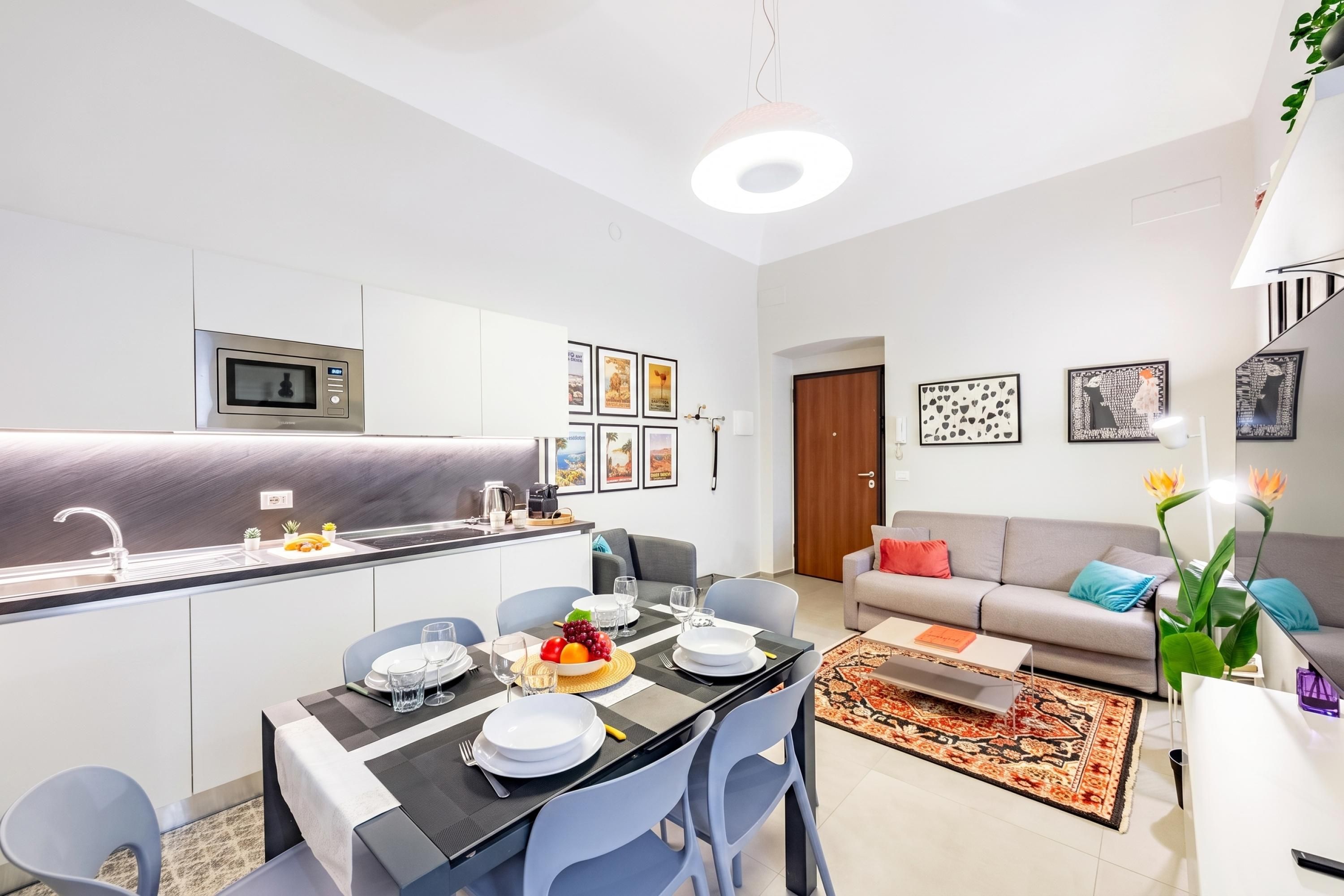 A modern kitchen with a built-in microwave, a dining area with a table set for two, and a living area with a sofa and a coffee table.