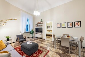 A modern living room with a sofa, ottoman, and a dining area with a table set for two. - Lovely Flat In Genova Historic Center Apartments (Genoa)