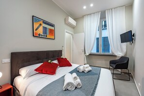 A modern hotel room with a large bed, a flat-screen TV, a chair, and a window with curtains. - Lovely Flat In Genova Historic Center Apartments (Genoa)