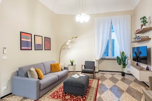 Un salon moderne comprenant un canapé, un fauteuil, un pouf et une grande fenêtre avec des rideaux.