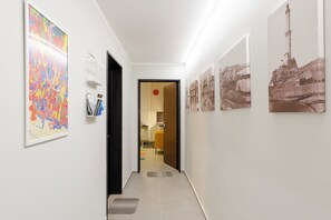 A hallway with artwork on the walls, a door leading to a room, and a tiled floor. - Lovely Flat In Genova Historic Center Apartments (Genoa)