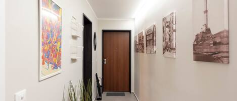 A hallway with a wooden door, framed artwork on the walls, and a potted plant.