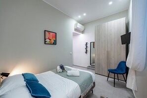Een moderne slaapkamer met twee bedden, een flatscreen televisie, een spiegel en een blauwe stoel.