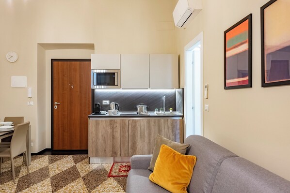 A compact living space with a kitchenette, a sofa with a yellow pillow, and a patterned rug. - Lovely Flat In Genova Historic Center Apartments (Genoa)