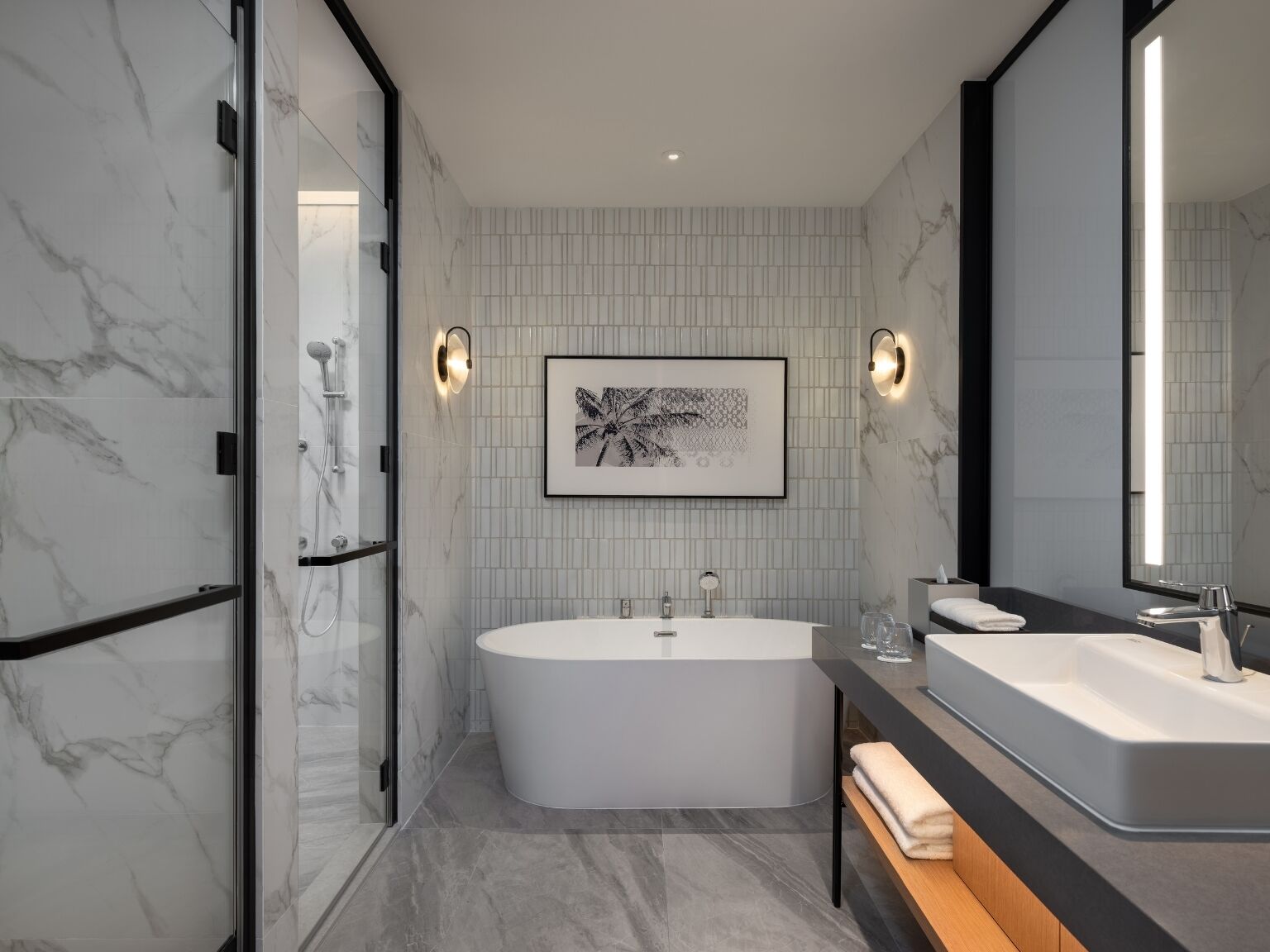 A modern bathroom with a freestanding bathtub, a large mirror, and a framed artwork on the wall.