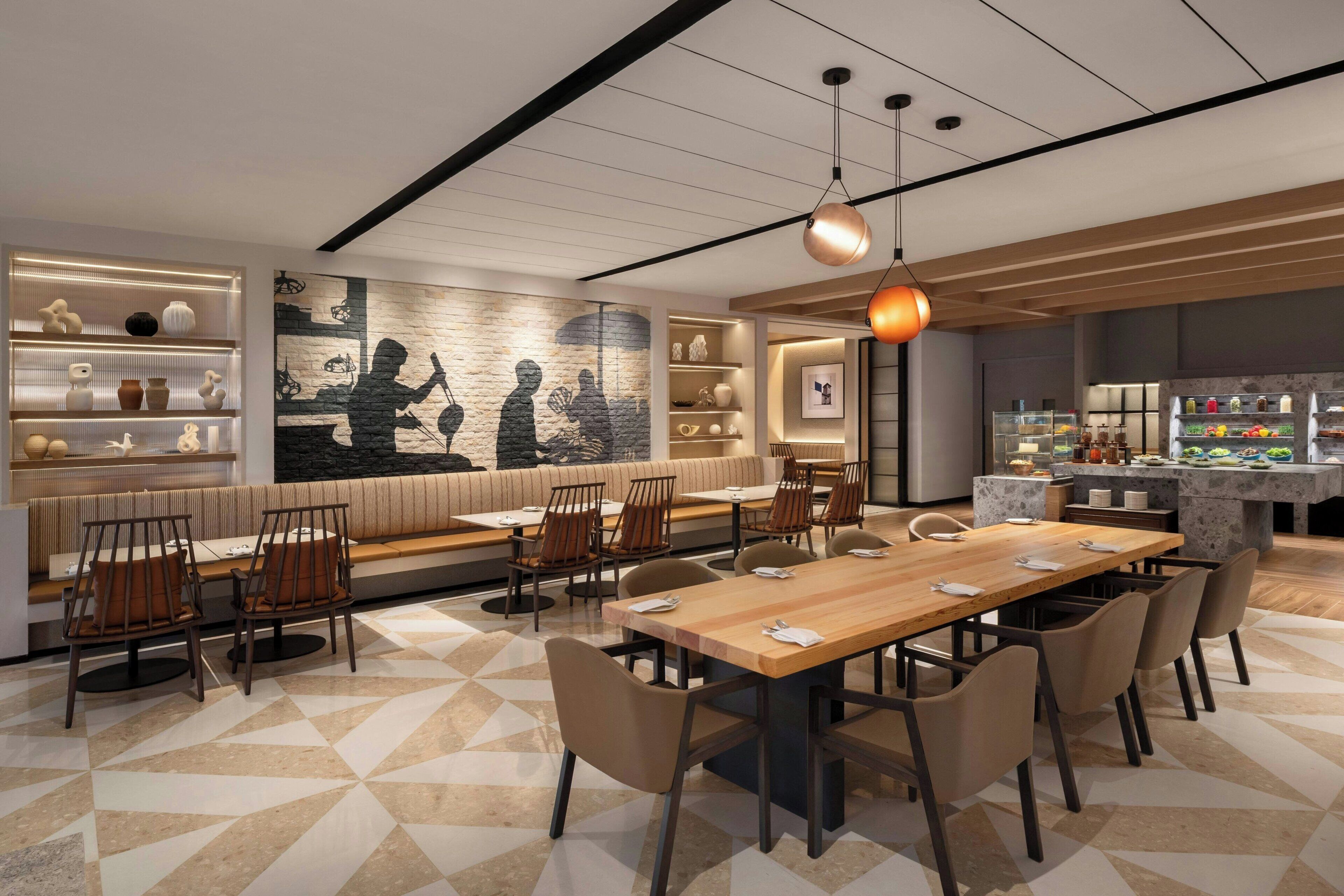 Un restaurante moderno con una larga mesa de madera, asientos acolchados y una pared decorativa con siluetas.
