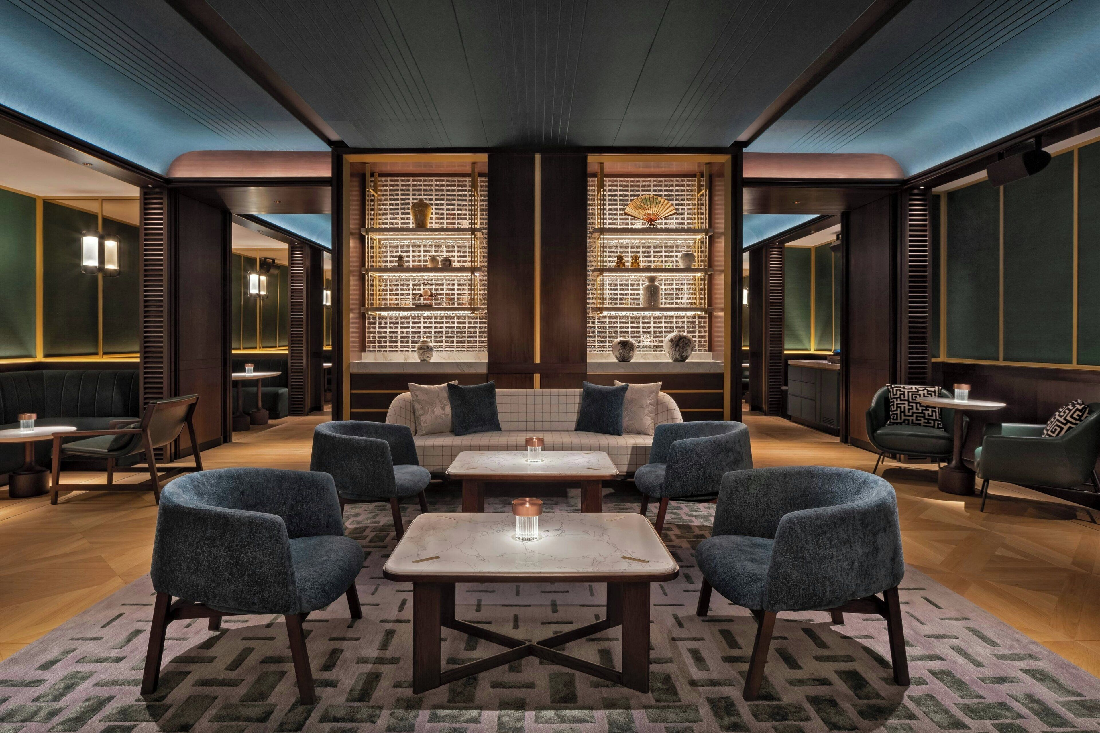 A modern lounge area with a central seating arrangement, a bookshelf, and a patterned carpet.