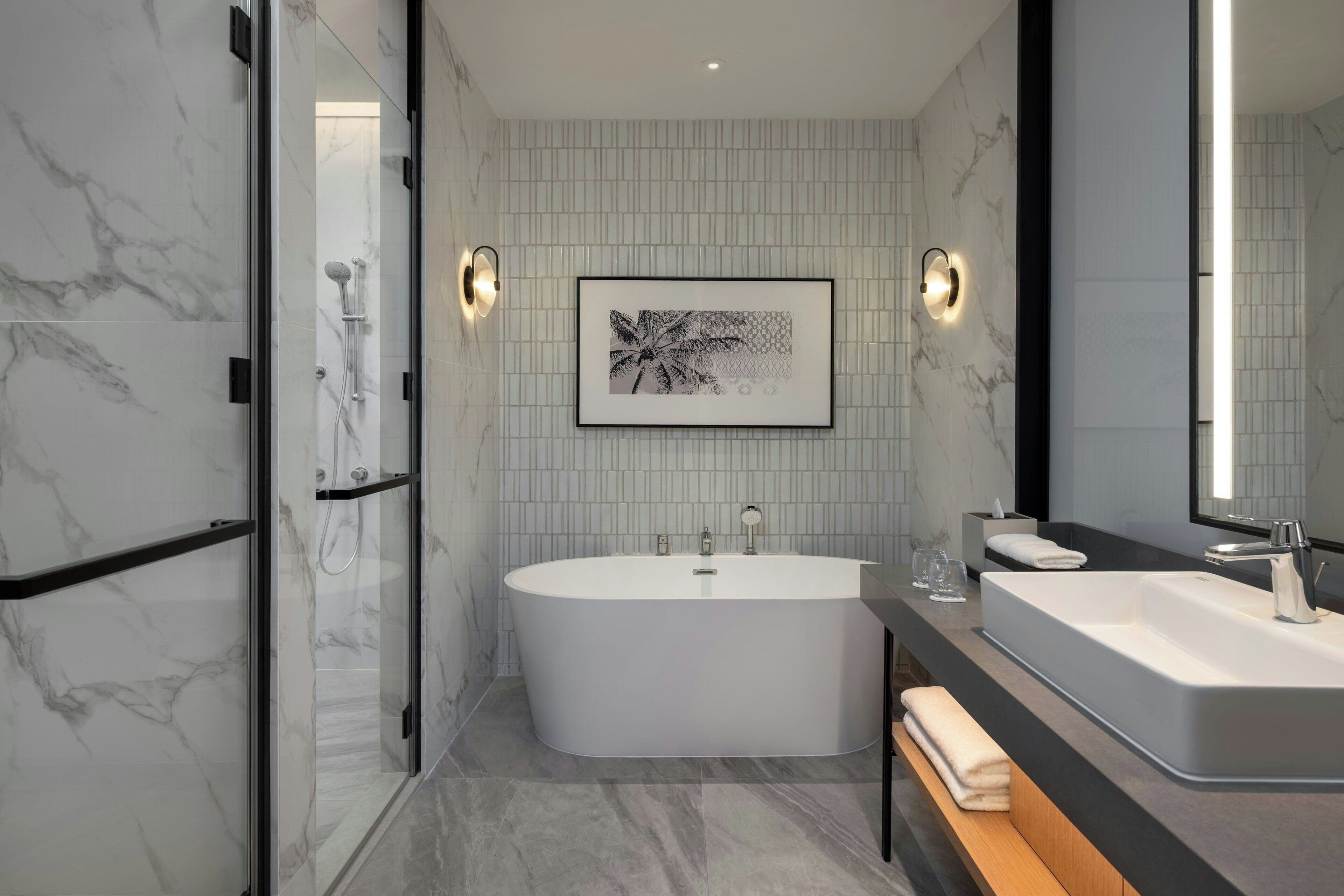 A modern bathroom with a freestanding bathtub, a large mirror, and a framed artwork on the wall.