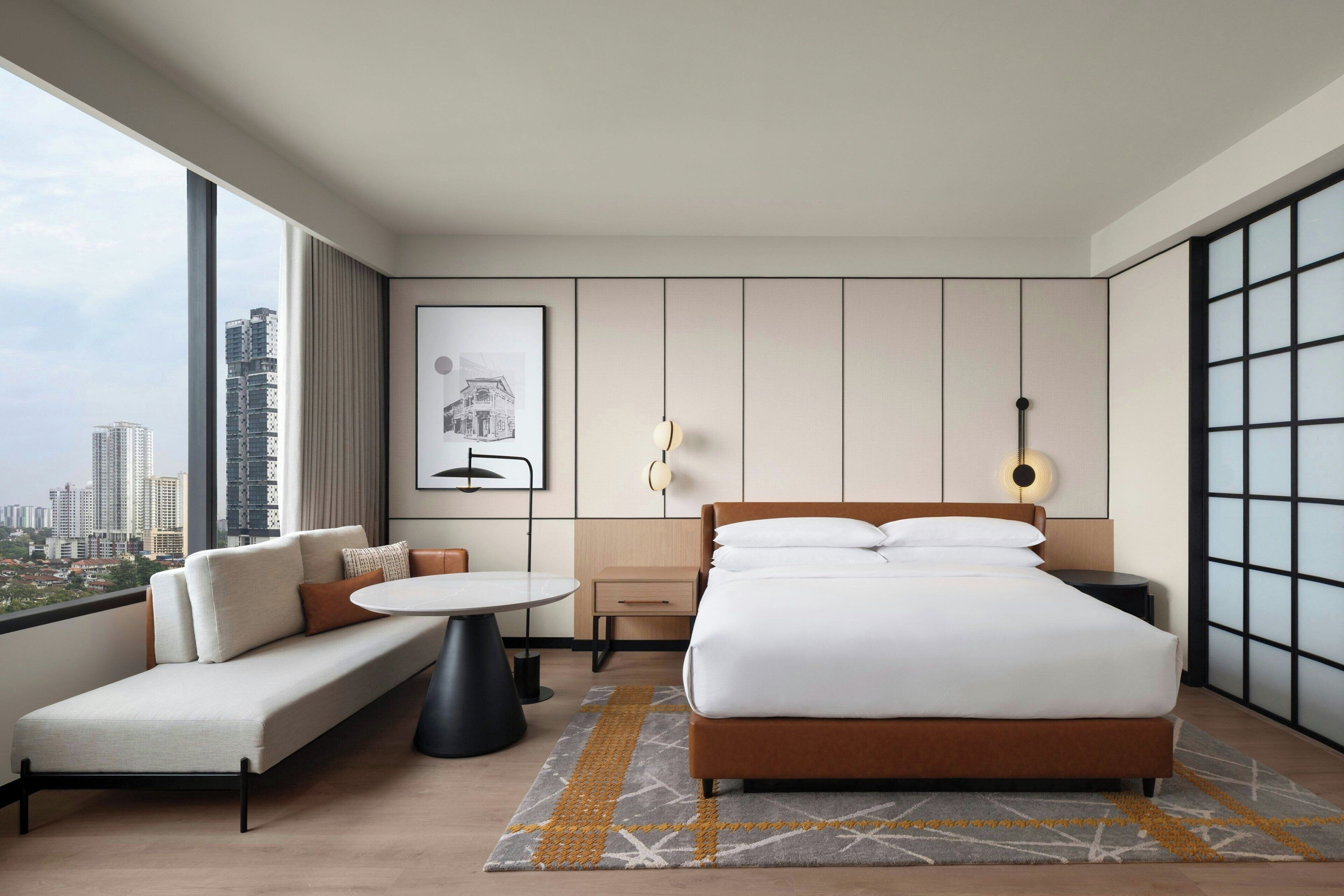 Una habitación de hotel moderna con una cama grande, un sofá, una mesita y vistas al horizonte de la ciudad.