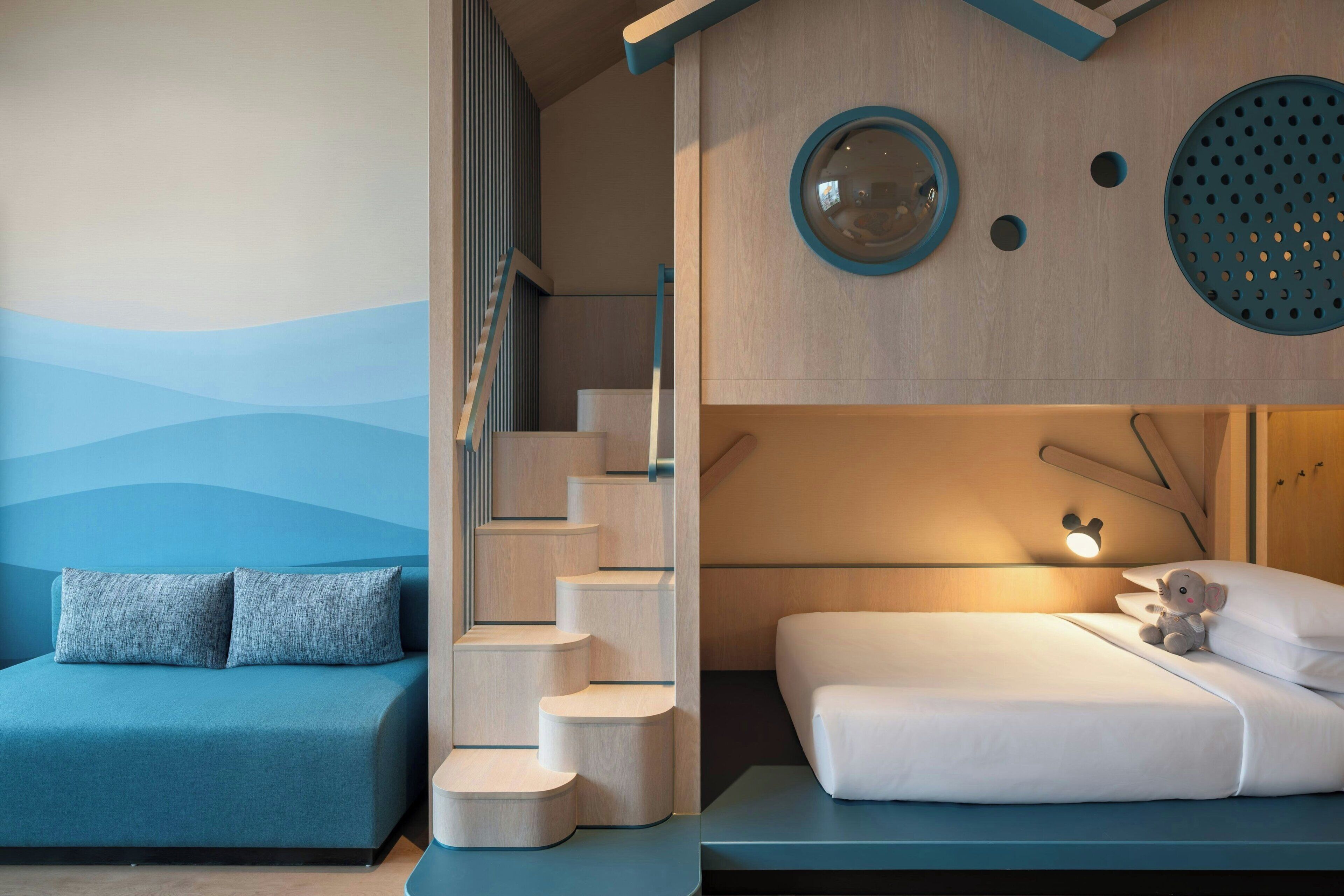 A modern bedroom with a built-in staircase, a bed with a Mickey Mouse lamp, and a blue sofa.