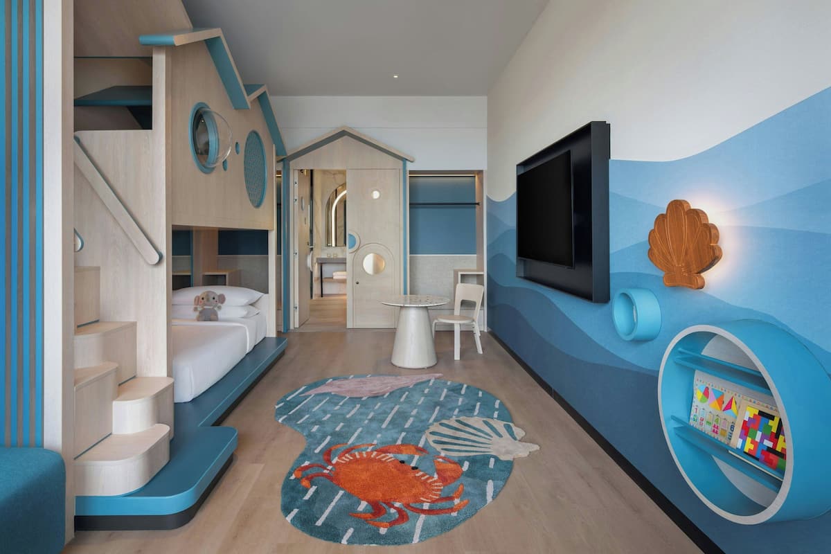 Une salle de jeux pour enfants sur le thème de la mer, comprenant une maisonnette, un tapis orné de motifs marins et une étagère murale remplie de jouets.