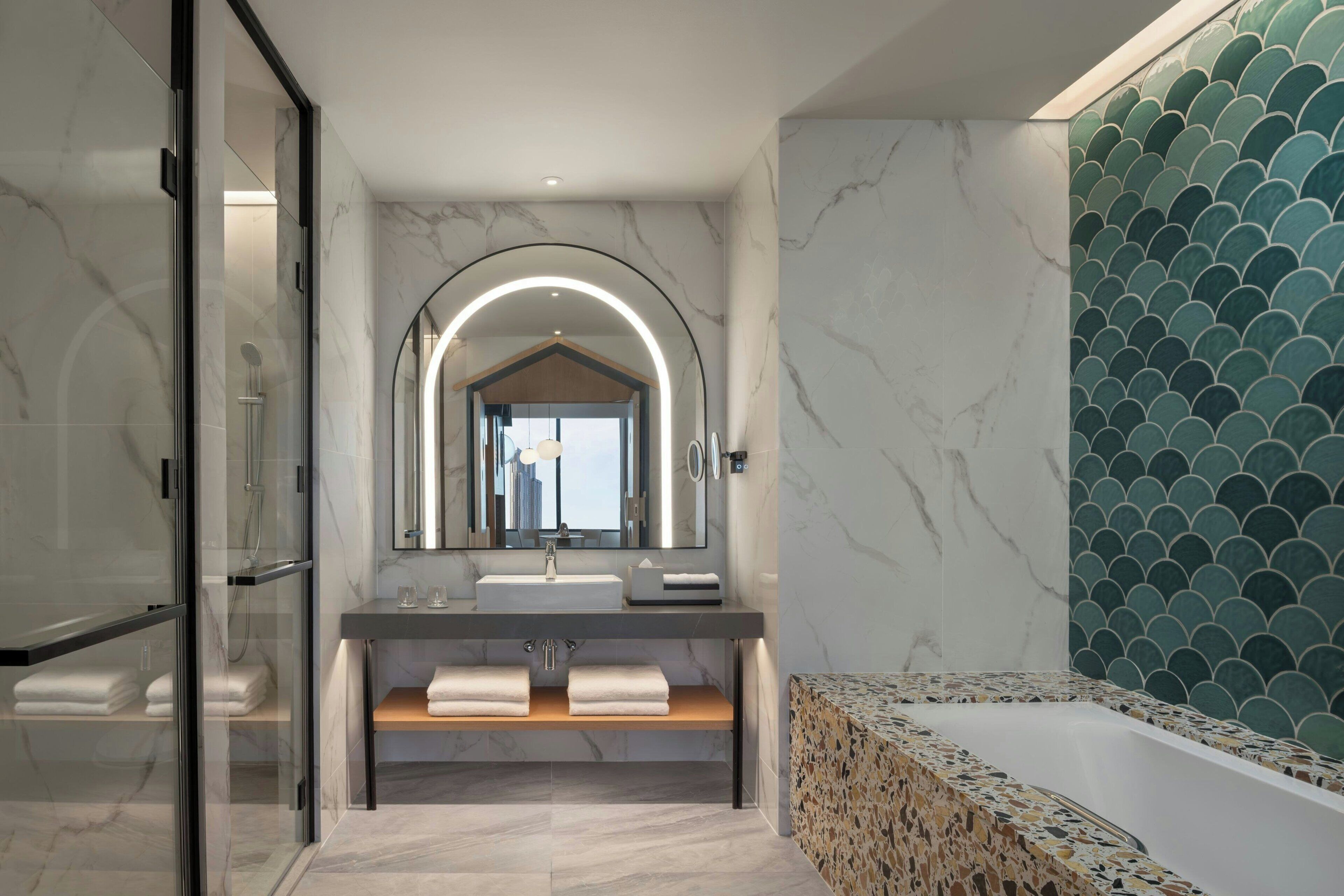 A modern bathroom with a glass-enclosed shower, a vanity with a marble countertop, and a bathtub with a mosaic tile surround.