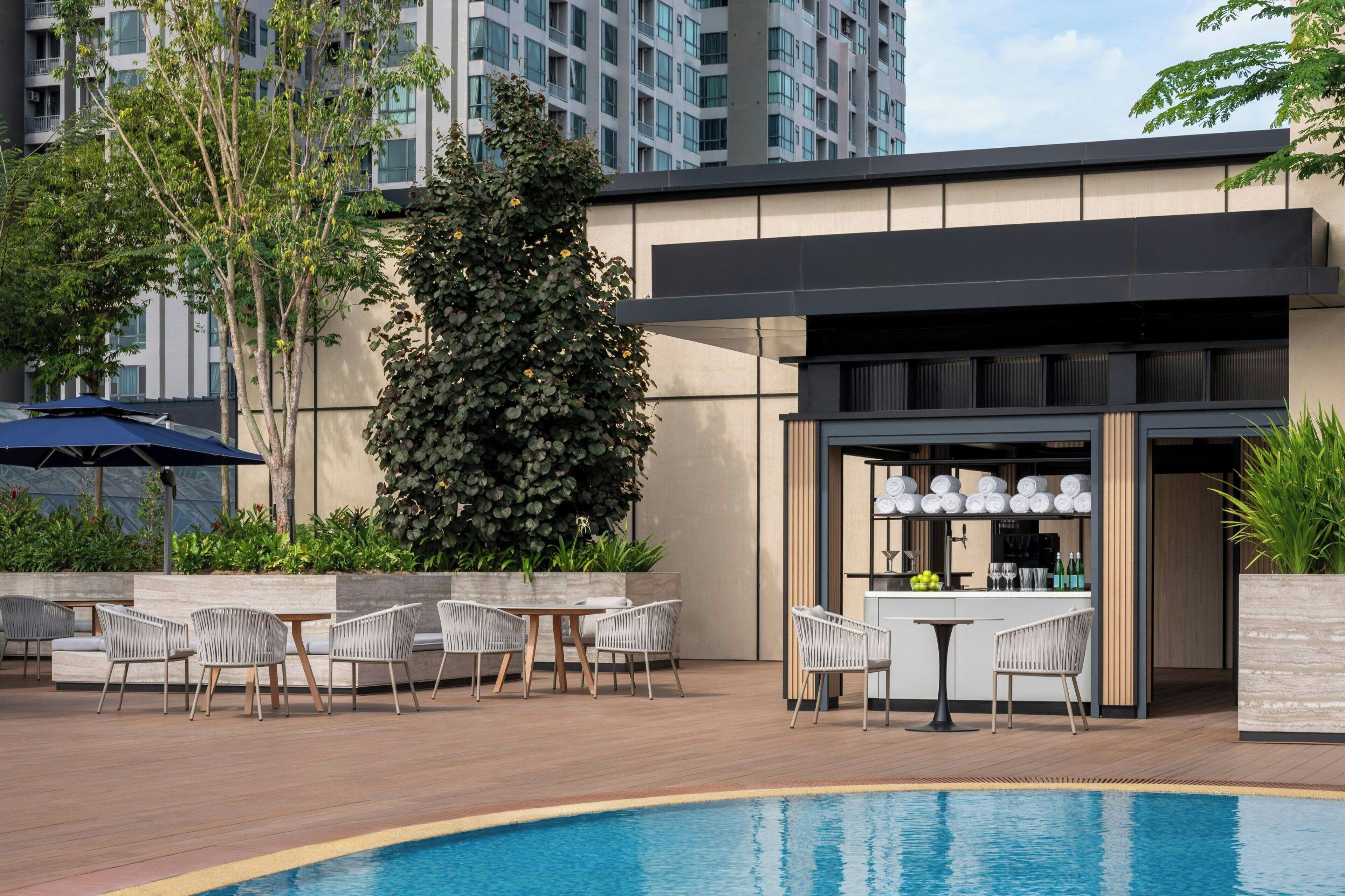 A poolside area with outdoor seating, a bar, and a view of a modern building in the background.