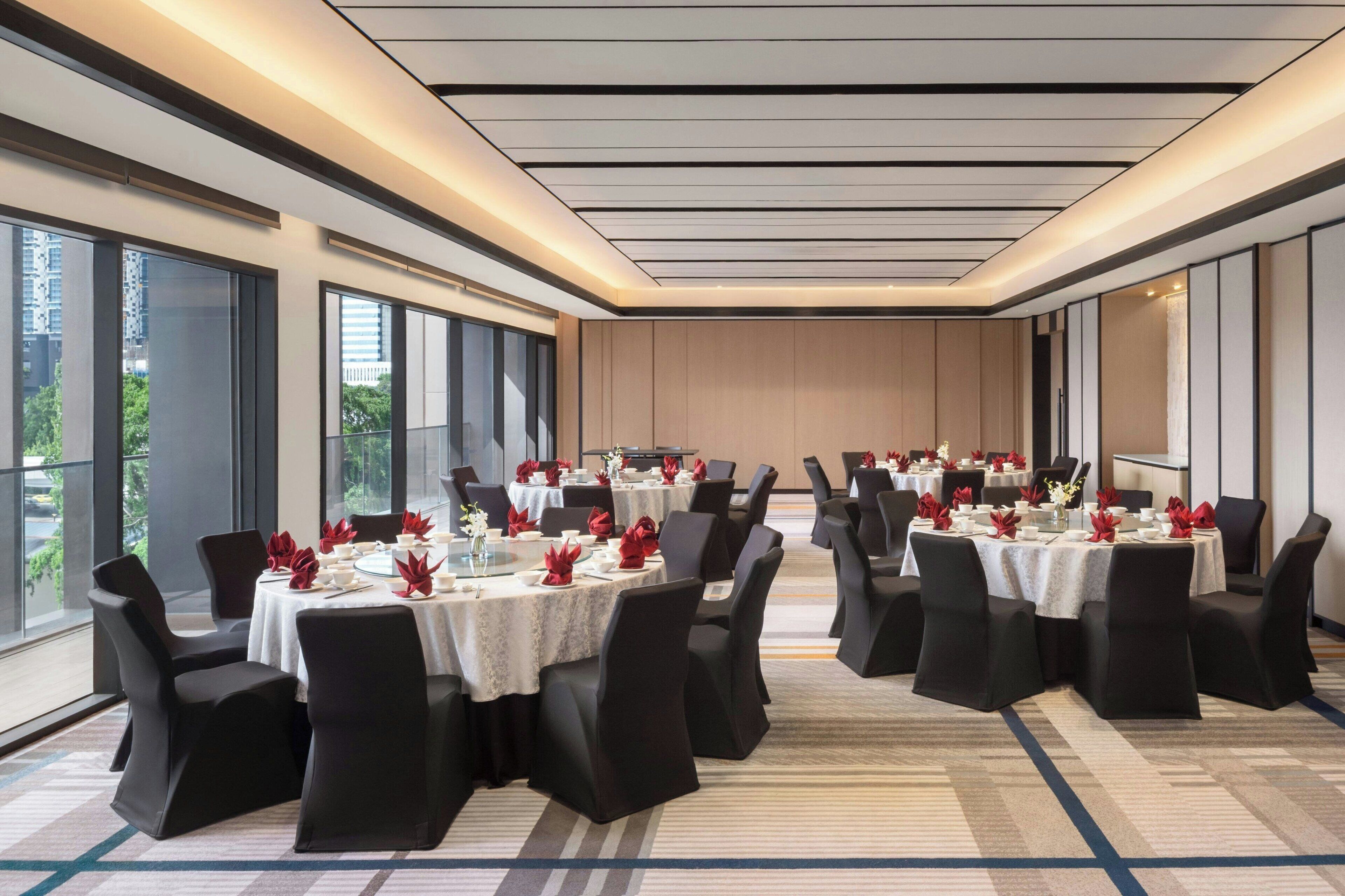 A conference room with multiple round tables, black chairs, and red floral centerpieces.