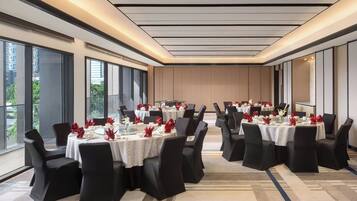 A conference room with multiple round tables, black chairs, and red floral centerpieces.