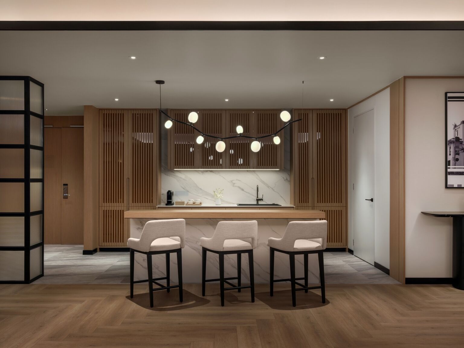 A modern kitchen with wooden cabinetry, a marble countertop, and three bar stools.