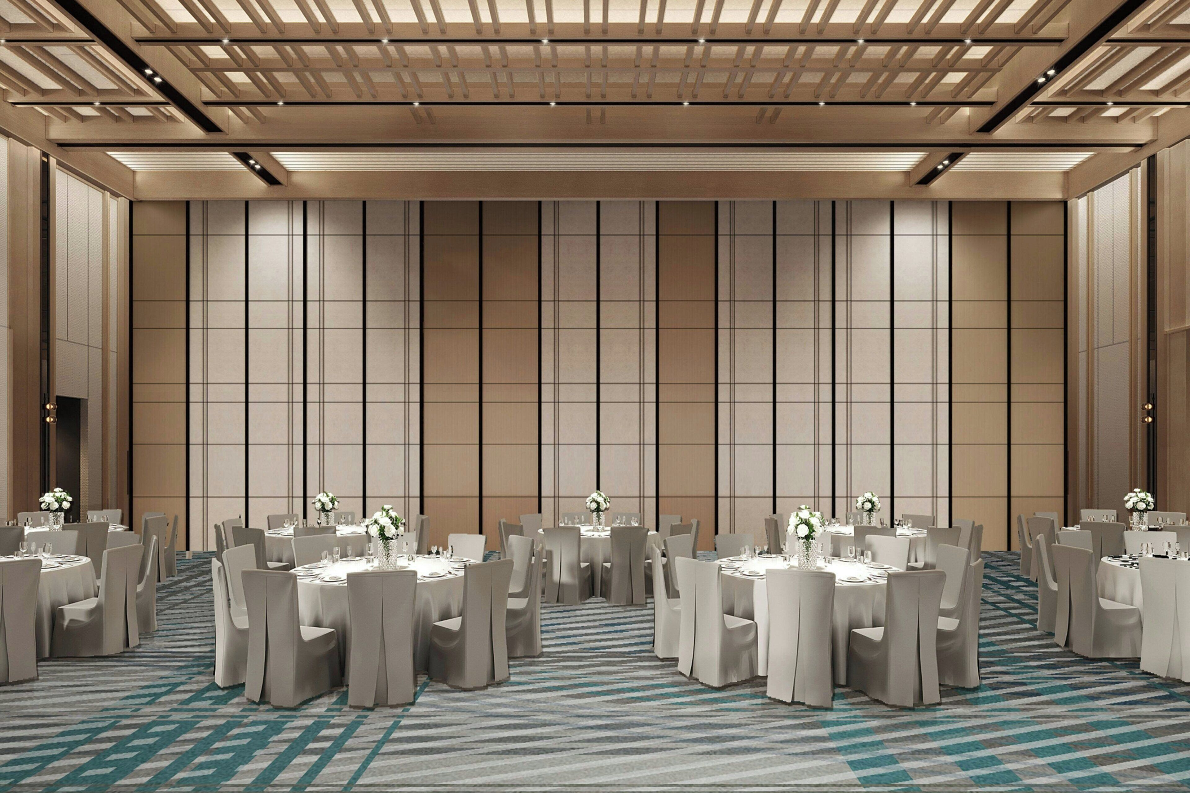 A spacious conference room with multiple round tables and chairs, a patterned carpet, and a high ceiling with recessed lighting.