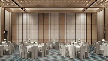 A spacious conference room with multiple round tables and chairs, a patterned carpet, and a high ceiling with recessed lighting.