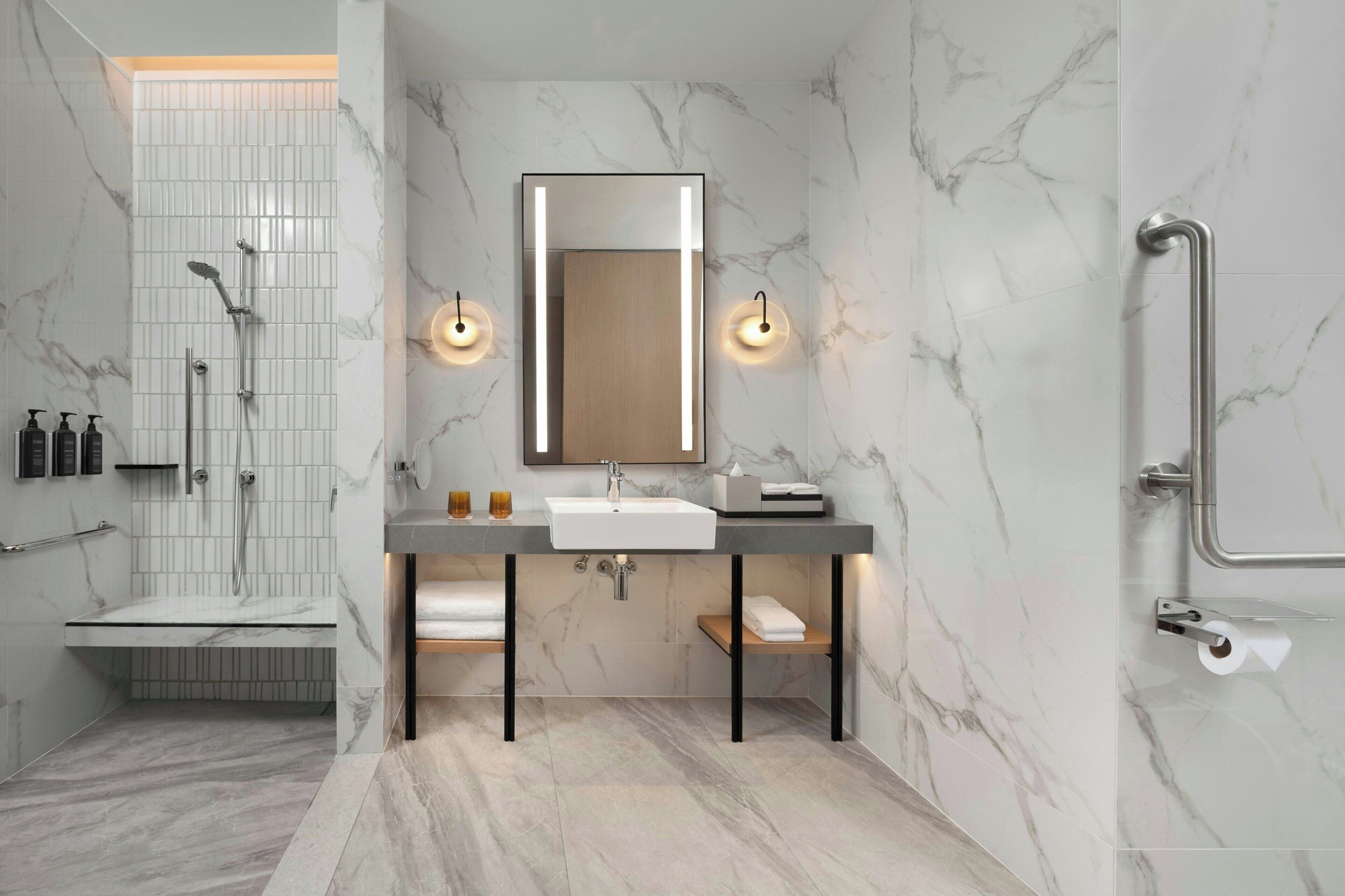 A modern bathroom with a marble backsplash, a large mirror, a sink, and a shower area.