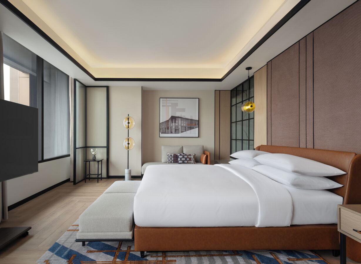 A modern hotel room with a large bed, a television, a small table, and a large window.