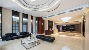 Un hall d’entrée spacieux, avec un canapé en cuir noir, une table basse en marbre et un comptoir d’accueil.
