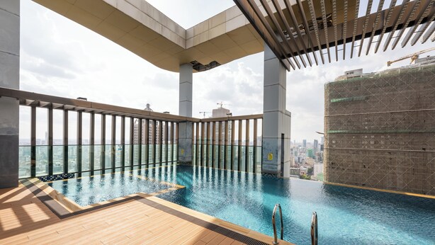 Une piscine à débordement intérieure dotée d’une terrasse en bois, entourée d’une rambarde en verre, et offrant une vue sur le paysage urbain.