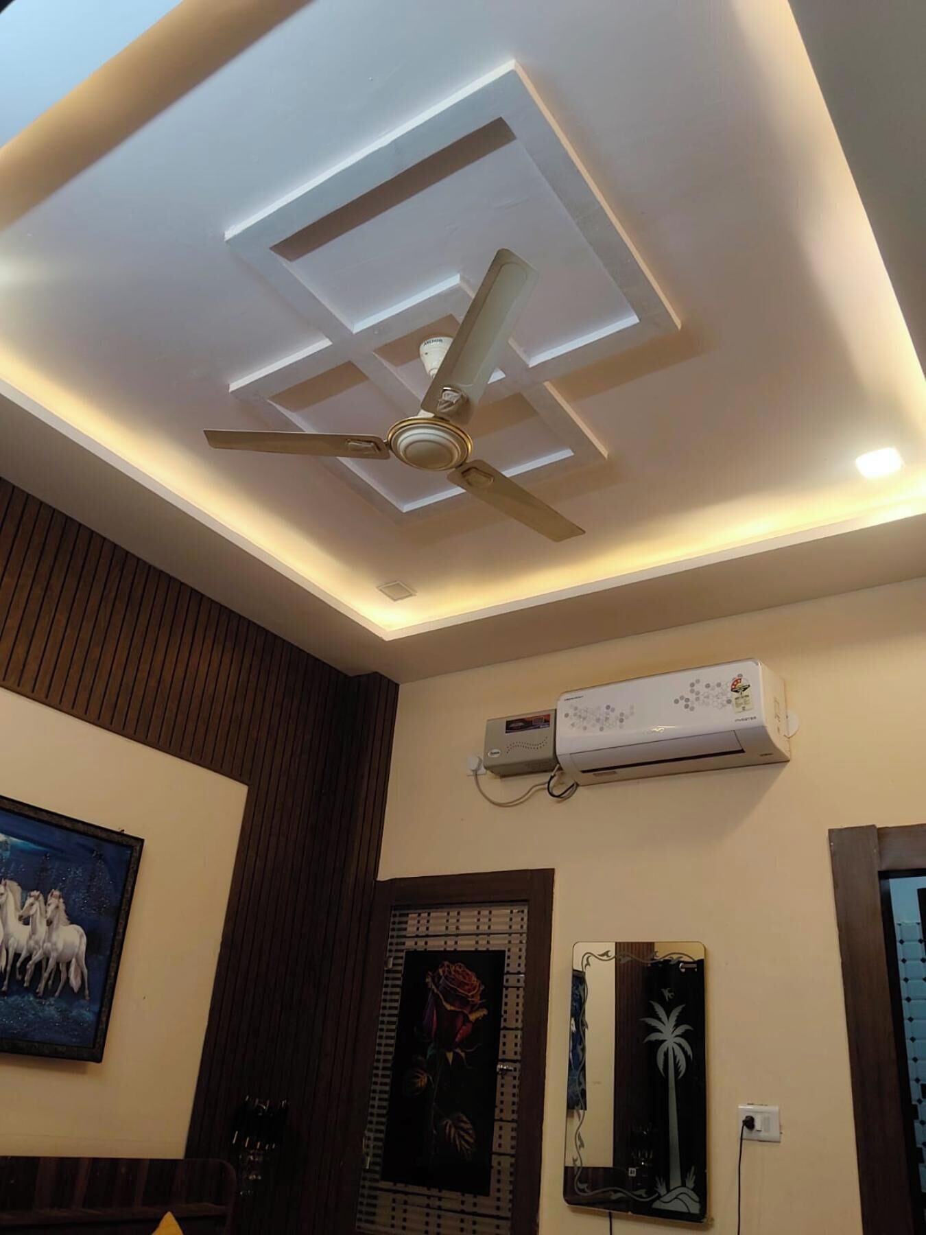 A ceiling with recessed lighting and a ceiling fan, an air conditioning unit, and artwork on the walls.
