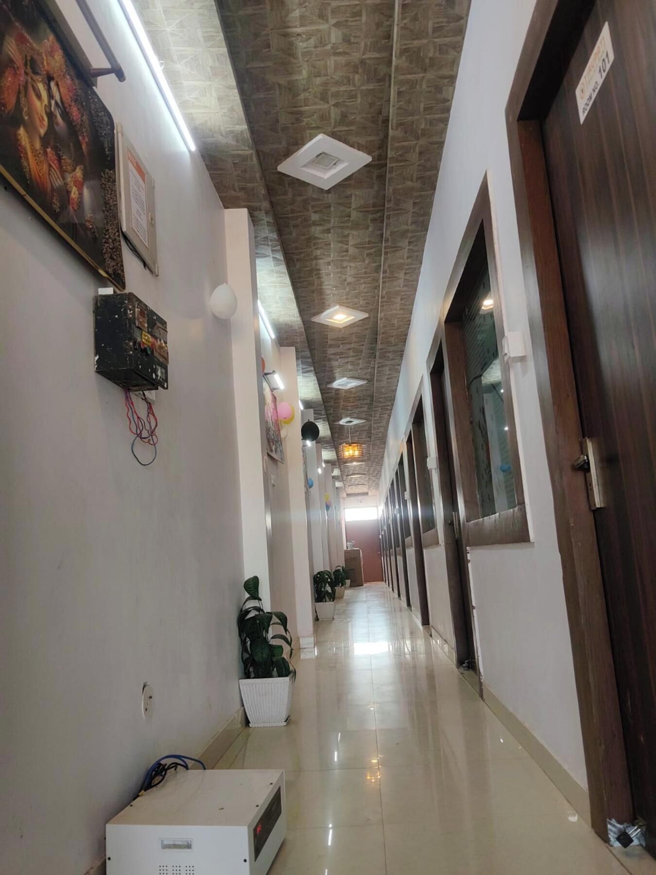 A long, well-lit hallway with a tiled floor, a ceiling with a stone-like pattern, and a door on the right.