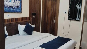 A neatly made bed with a blue and white bedspread, a wooden headboard, and a painting of white horses on the wall. - Tirupati Balaji Inn Bageshwar Dham (Rajnagar)