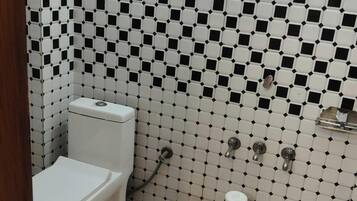 Un bany amb un paviment de rajoles quadriculat en blanc i negre, un vàter, un rentapeus i una zona de dutxa.