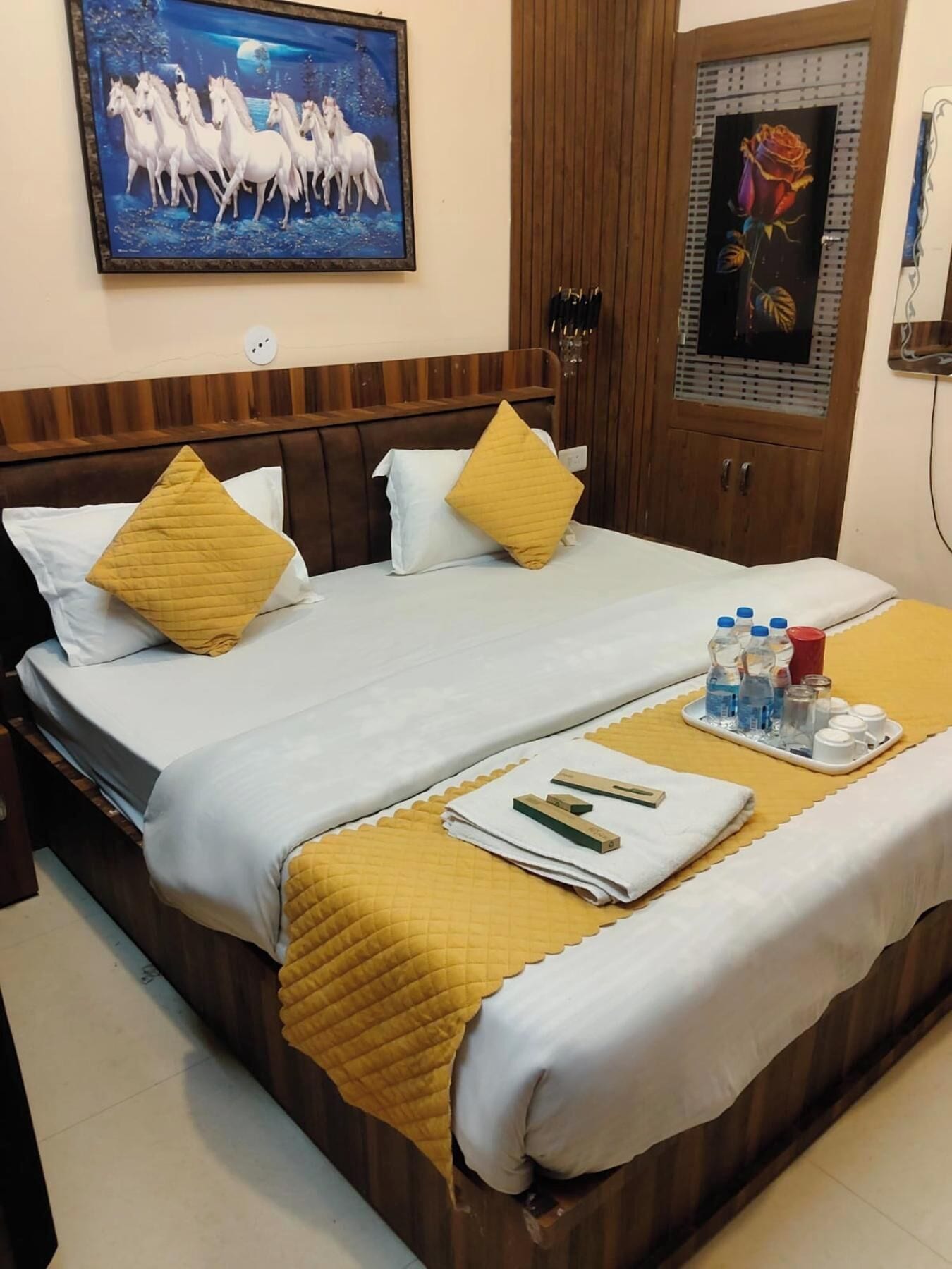 Habitación de hotel con cama, cabecero de madera, dos cuadros, armario de madera y una bandeja con artículos de aseo.